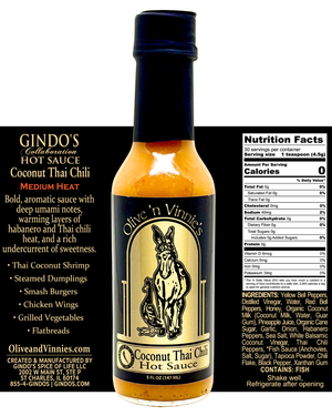 A bottle of Olive 'n Vinnie's Coconut Thai Chili Hot Sauce centered on a black background, with product details, ingredients, and nutrition facts printed on both sides. The bottle contains amber-orange sauce and has a black cap with a cream and black label featuring a donkey illustration.
