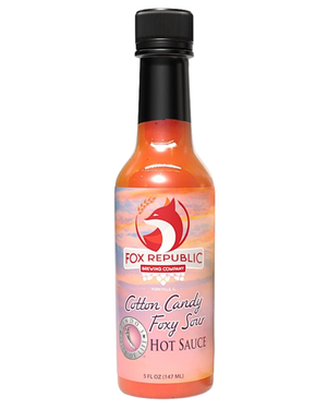 A bottle of Fox Republic 'Cotton Candy Foxy Sau' hot sauce, featuring a black cap and a label with a red fox logo and orange, pink, and purple gradient background, set against a plain white background.