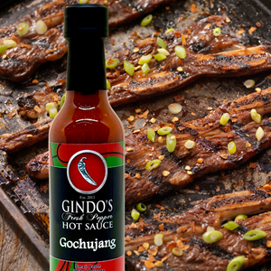Bottle of Gindo's Hot Sauce on a tray with grilled meat and vegetables