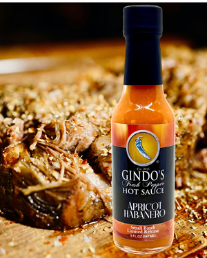 Bottle of Gindo's Apricot Habanero hot sauce with a brisket dish in the background
