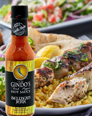 Bottle of Gindo's Belizean Jerk hot sauce with a plate of grilled chicken and rice in the background