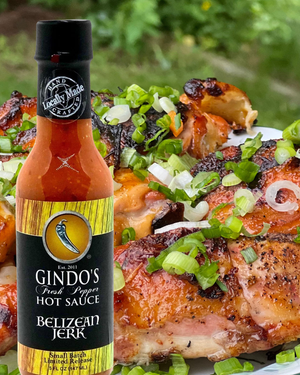 Gindo's Belizean Jerk hot sauce bottle with grilled chicken and green onions in the background
