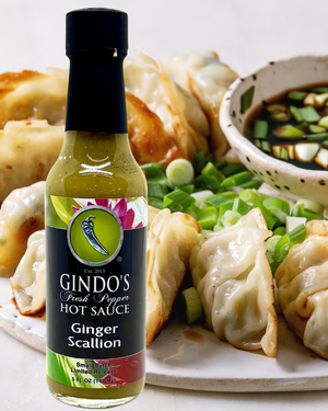 Bottle of Gindo's Ginger Scallion Hot Sauce with a plate of dumplings and dipping sauce in the background.