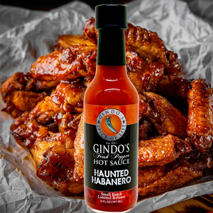 Gindo's Haunted Habanero hot sauce bottle with chicken wings on a textured surface