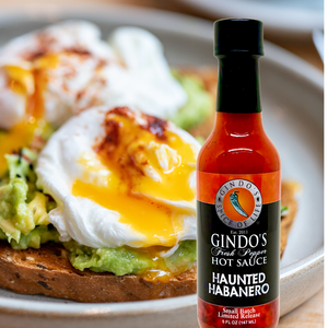 Bottle of Gindo's Haunted Habanero hot sauce with a plate of avocado toast and poached egg in the background.