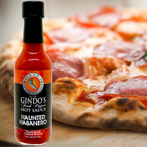 Bottle of Gindo's Haunted Habanero hot sauce with a pizza in the background