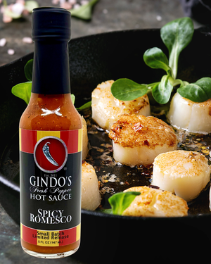 Bottle of Gindo's Spicy Romesco hot sauce with scallops in a pan