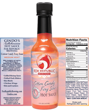 A bottle of Fox Republic Brewing Cotton Candy Foxy Saw Medium Heat hot sauce centered over a product information card. The bottle is filled with orange-red sauce and has a black cap.